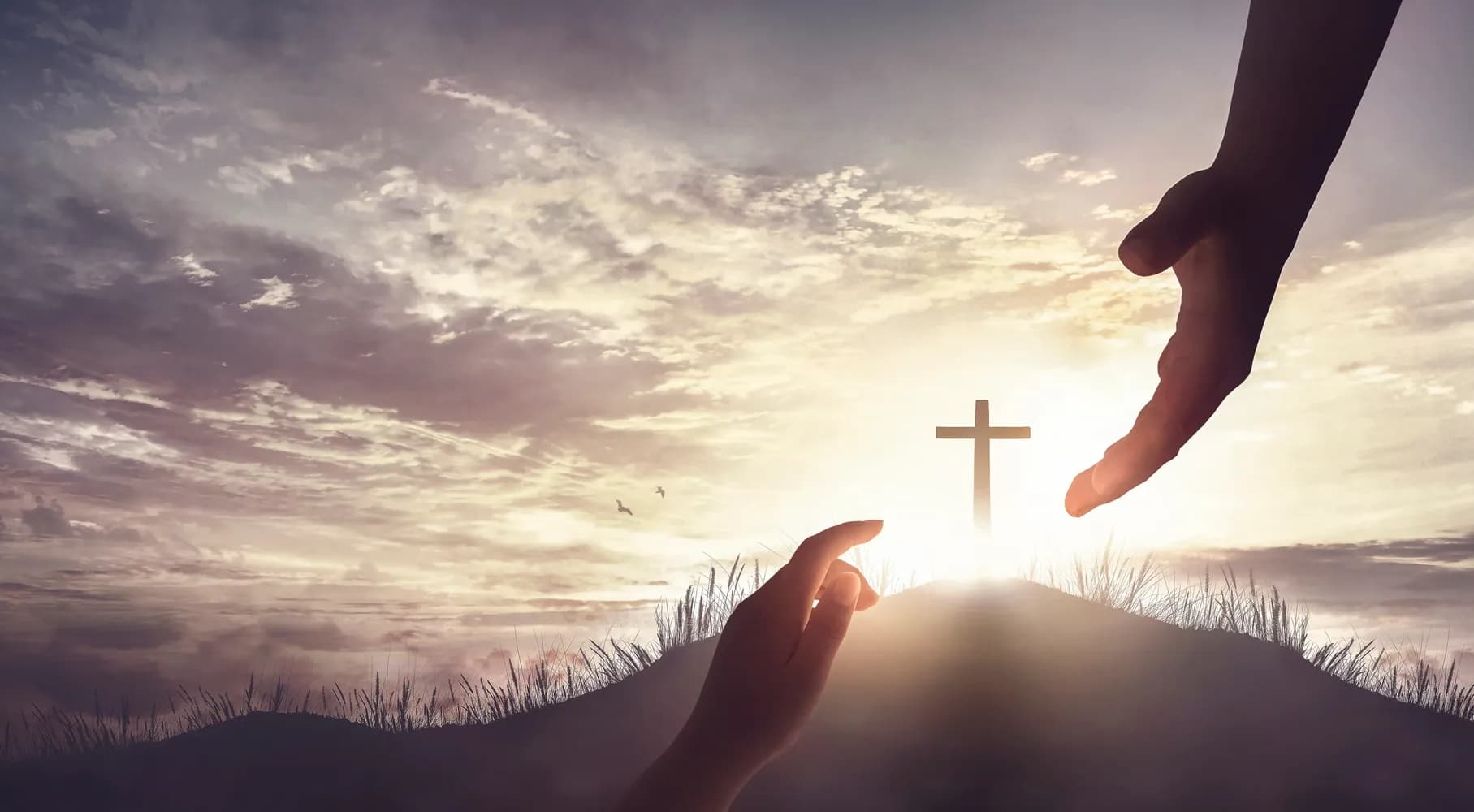 Hands reaching toward each other with cross and sunset